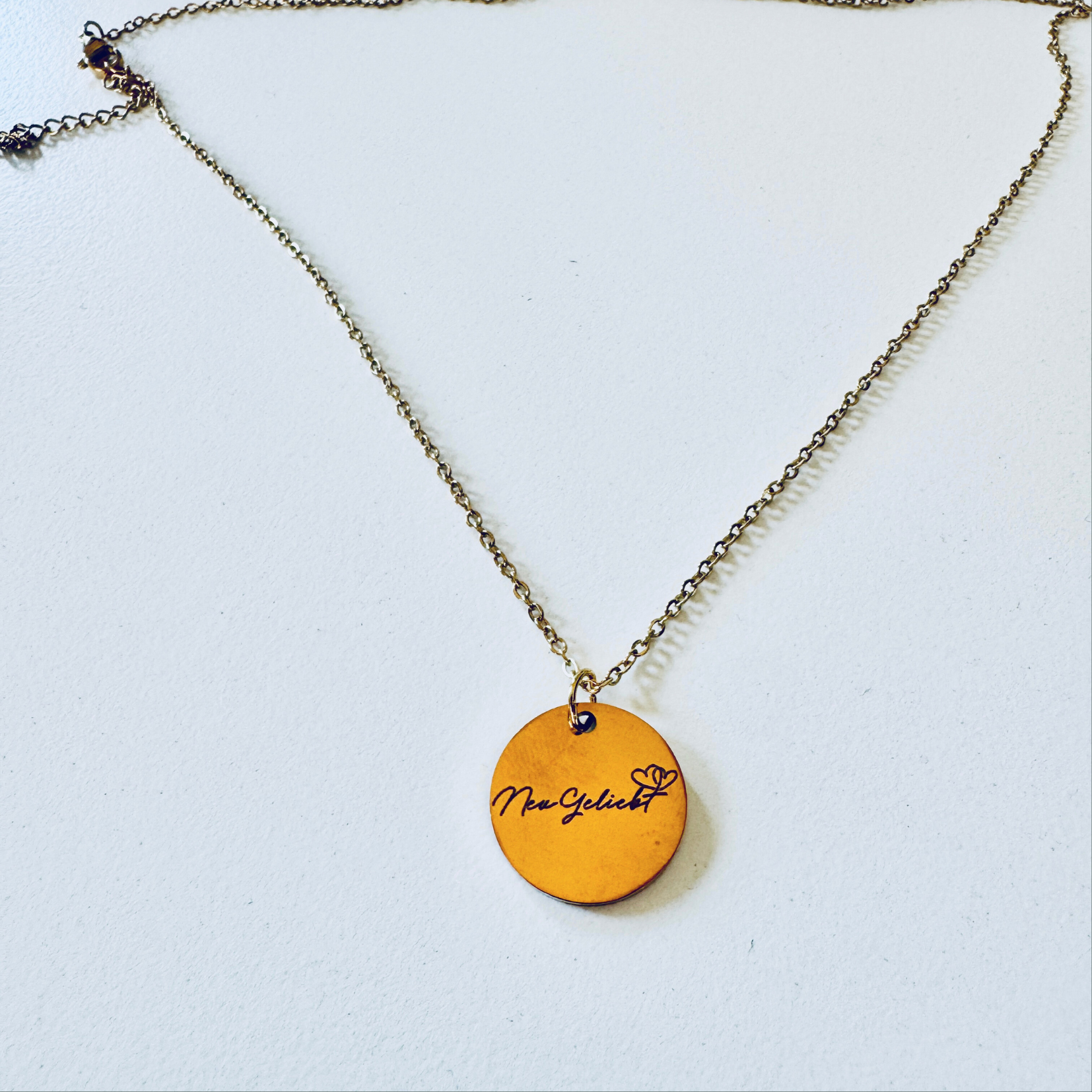 Anhänger mit langer Kette, goldfarben mit dem NeuGeliebt Logo.