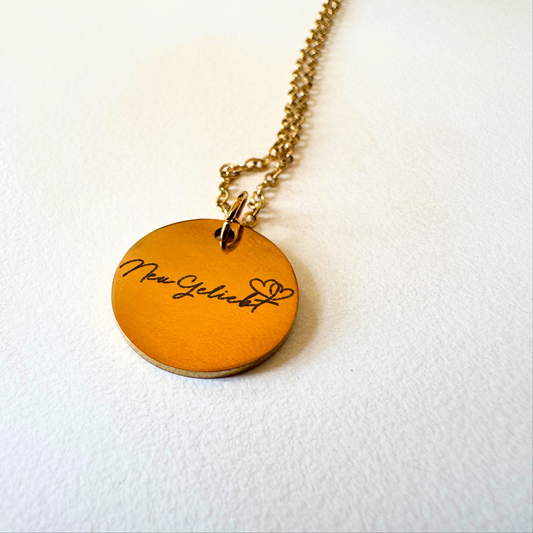 Anhänger mit Kette, goldfarben mit dem NeuGeliebt Logo., weißer Hintergrund.